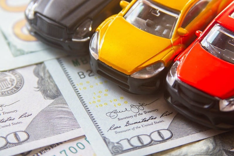 Red, yellow and black toy cars on top of 100 dollar bills for auto finance concept