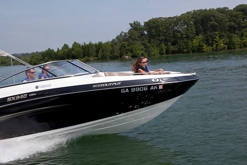 Dad drives speed boat with wife next to him and to kids at front of the boat smiling